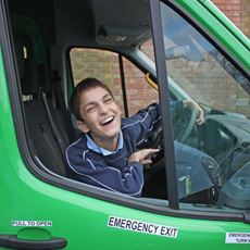 Little boy leaning out and laughing behind the wheel of a minibus